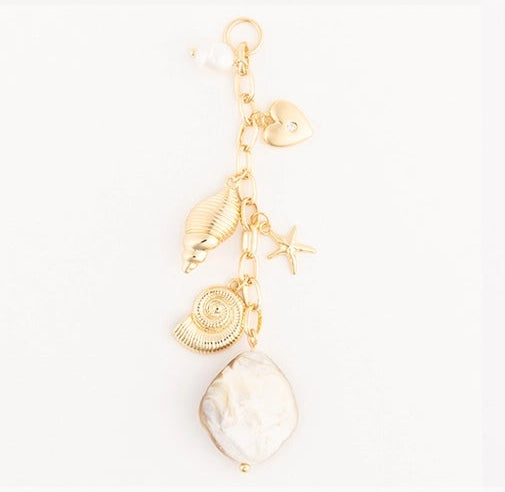 Nine gold-toned nautical-themed jewelry charms or earrings are arranged in a 3x3 grid on a white background. Designs include a feather, sailboat, anchor, shell, starfish, pearl bead strand, scallop, beaded strand with blue and white beads, and a seahorse.