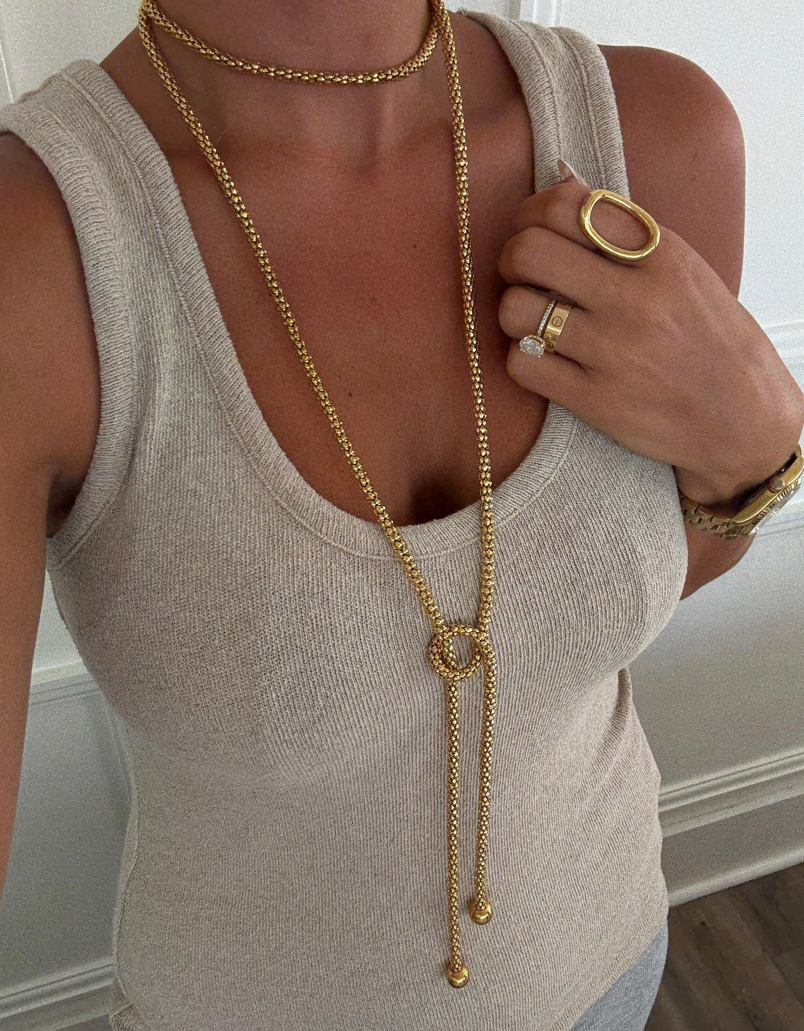Person wearing a beige tank top and gold jewelry including a necklace and ring.