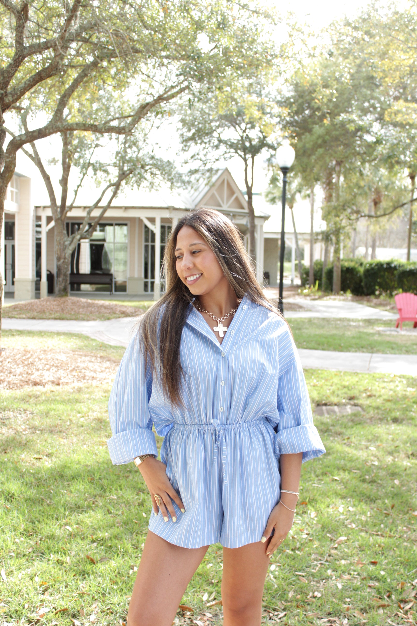 Woman in a blue dress standing outdoors with trees and a building in the background