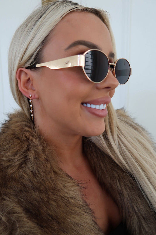 Woman wearing a fur coat with a neutral background, wearing gold/diamond drop earrings