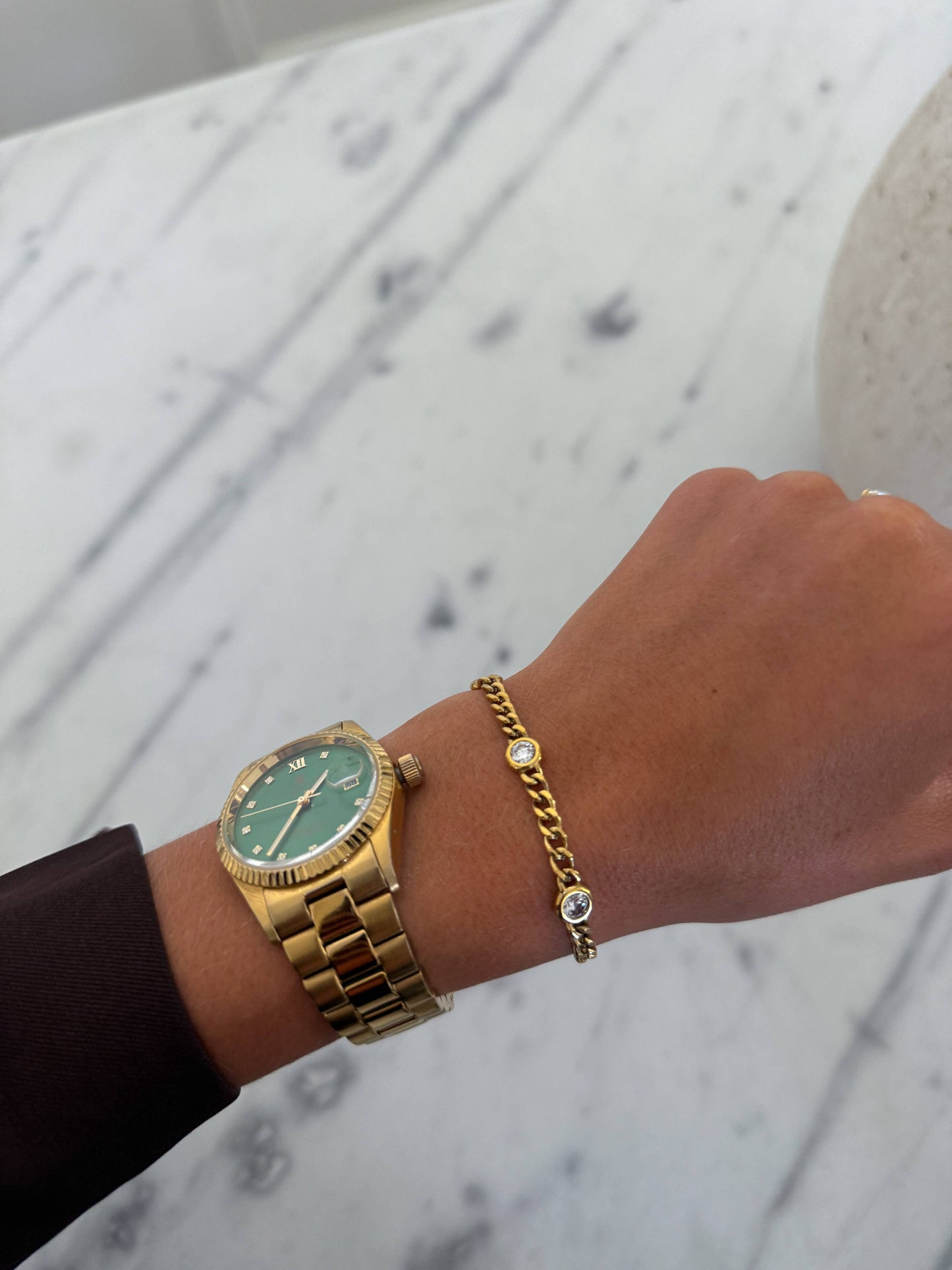 Gold watch and bracelet on a wrist with a marble background