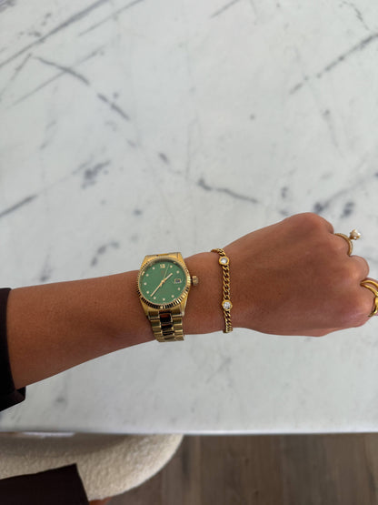 Hand wearing a gold watch and bracelet on a marble surface